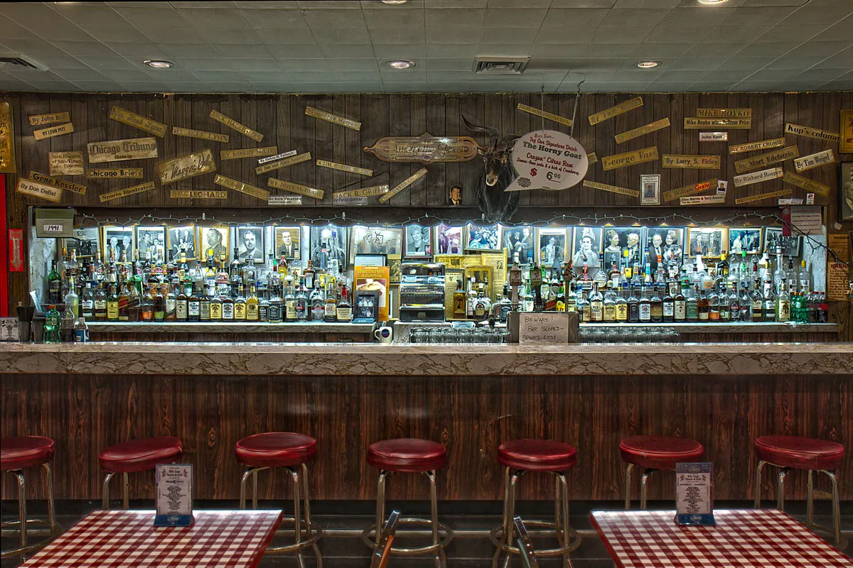 The long bar, red stools, and journalist nameplates at Billy Goat Tavern