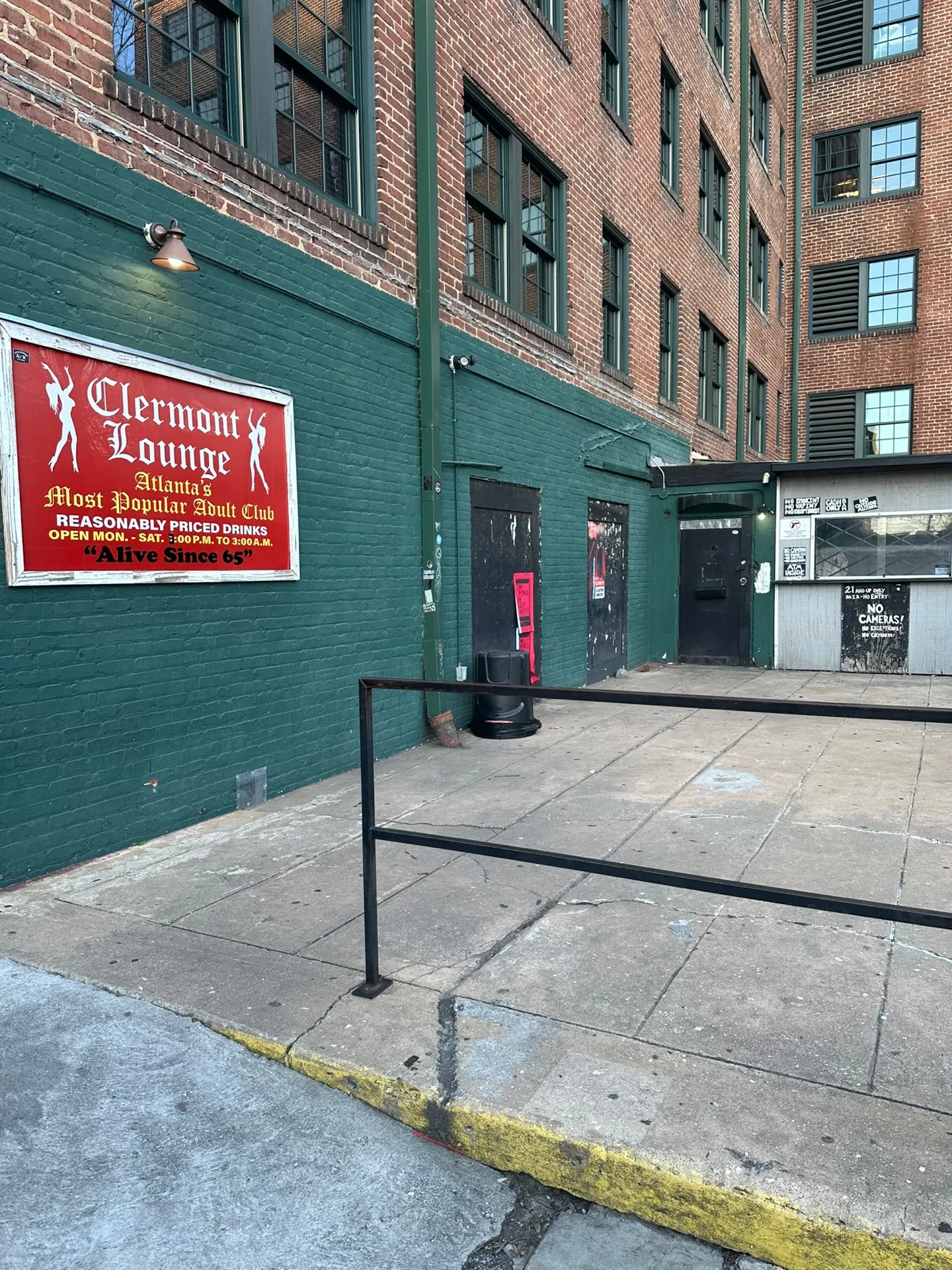 Green-brick alley entrance of Clermont Lounge with the red Atlanta adult-club hours board