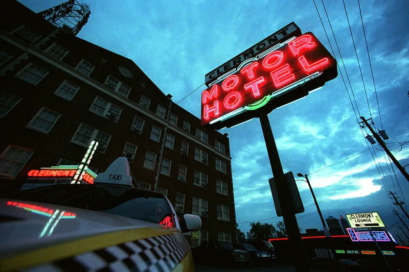 Clermont Motor Hotel red neon and Clermont Lounge signs at dusk with a yellow taxi in the foreground