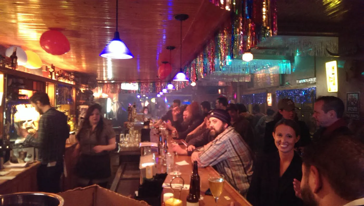 The long wooden rail, hanging lights, and packed stools inside Four Moon Tavern