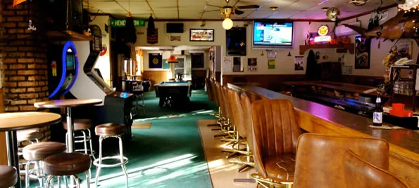 The Four Treys bar rail, stools, and green carpet looking toward the pool table