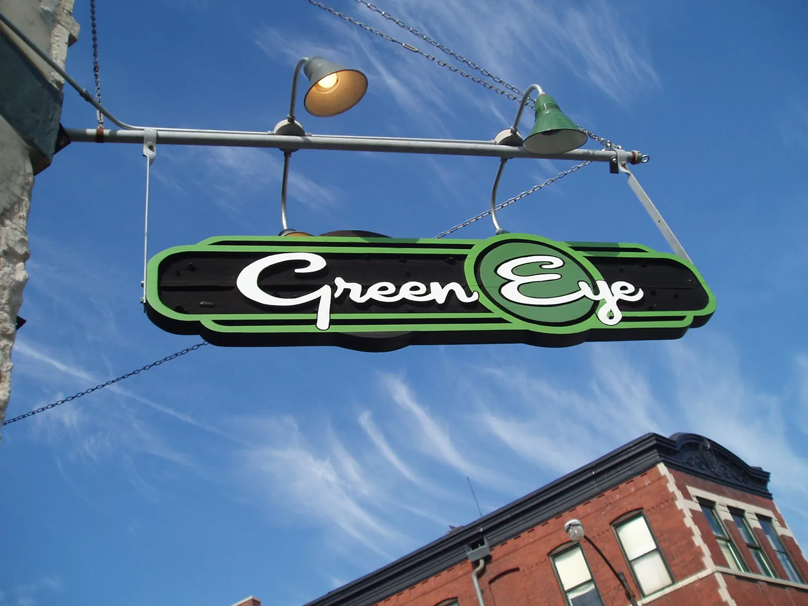 The hanging Green Eye sign with gooseneck lamps against a Chicago brick building