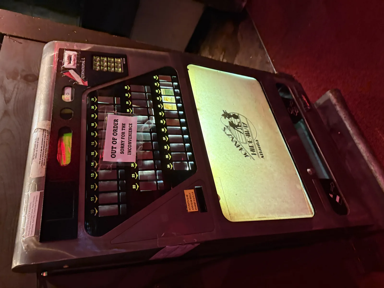 Vintage cigarette machine lit with the Johnny's Hideaway Atlanta logo, out-of-order note taped over the selection buttons
