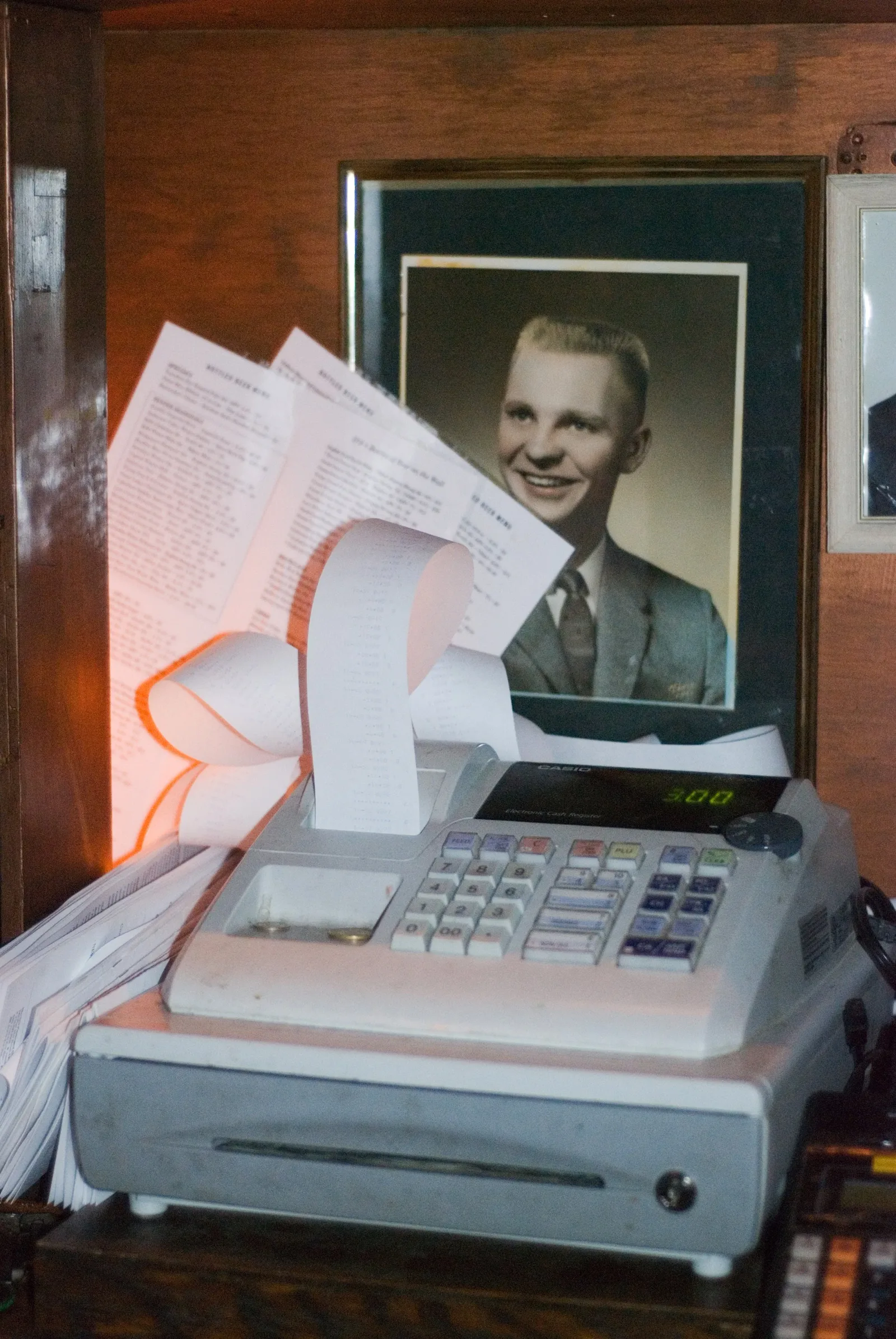 A Casio register showing $3.00 and a bottled-beer menu at Maria's Packaged Goods & Community Bar
