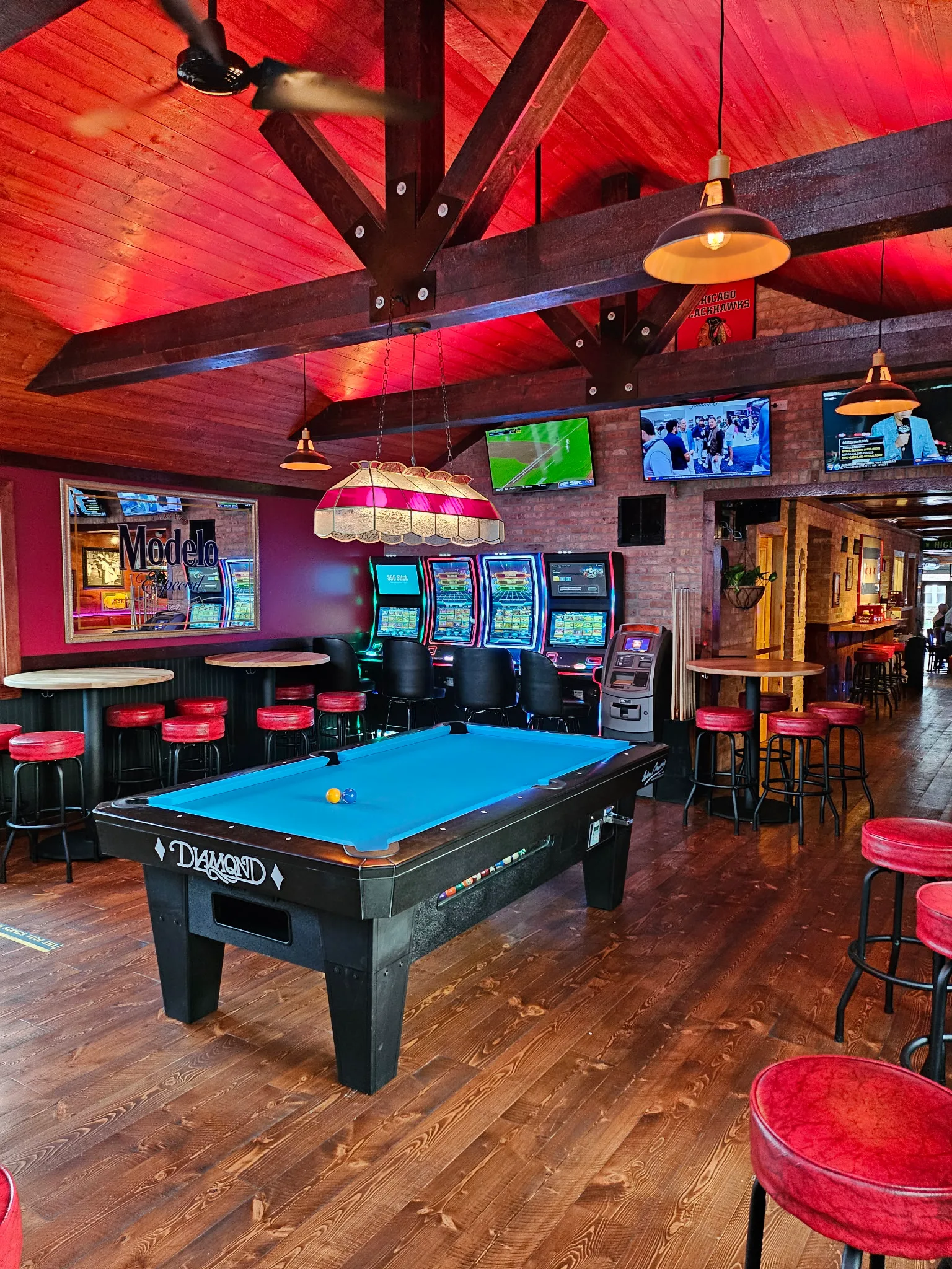 The pool table, red stools, exposed brick, and timber rafters inside Tommy's on Higgins