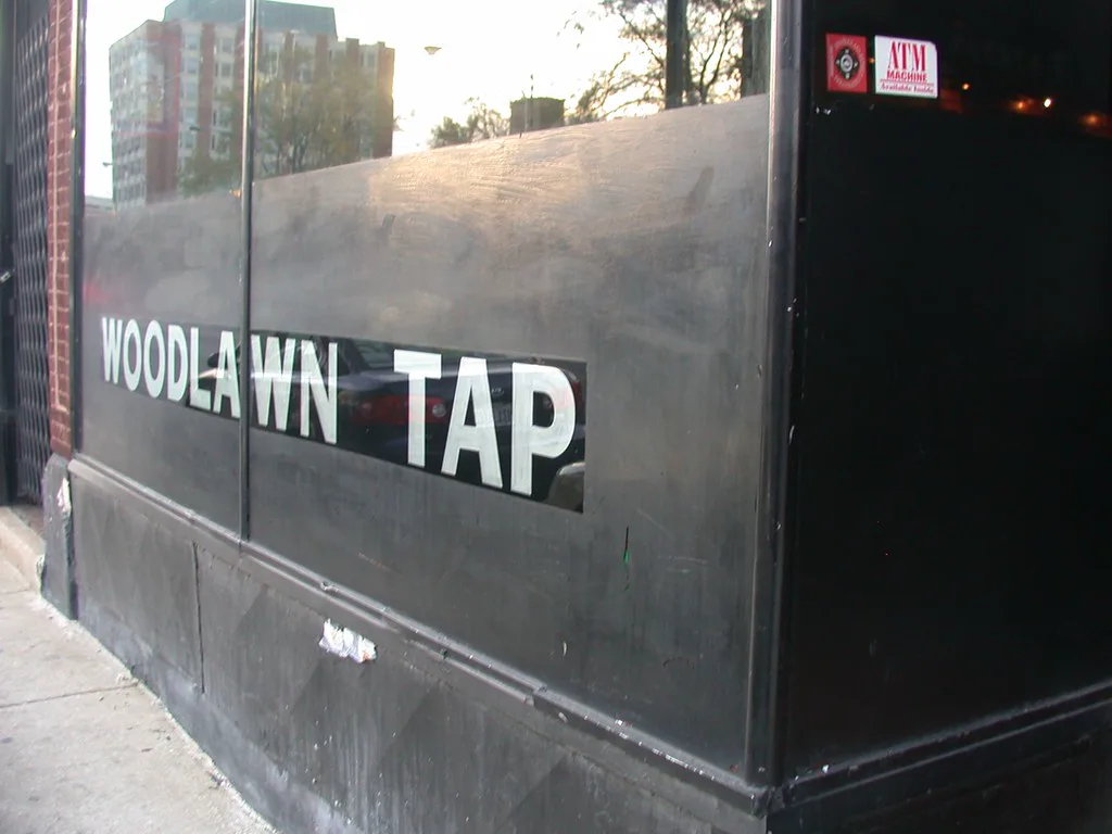 Woodlawn Tap lettered in a blacked-out storefront window on 55th Street